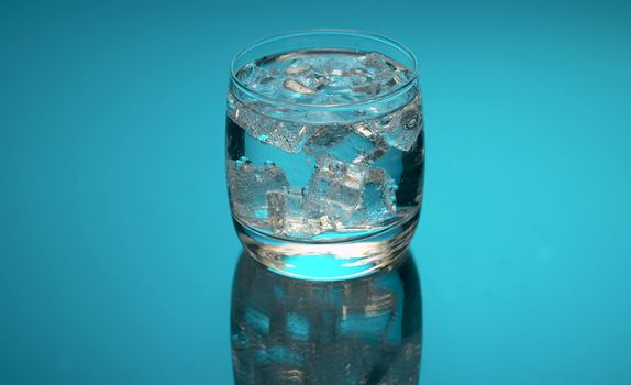 Close up tonic, soda sparkling water in a glass with ice on a blue background. Refreshing mineral water.