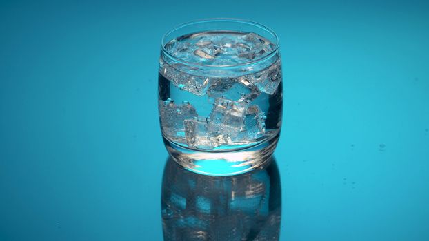 Close up tonic, soda sparkling water in a glass with ice on a blue background. Refreshing mineral water.