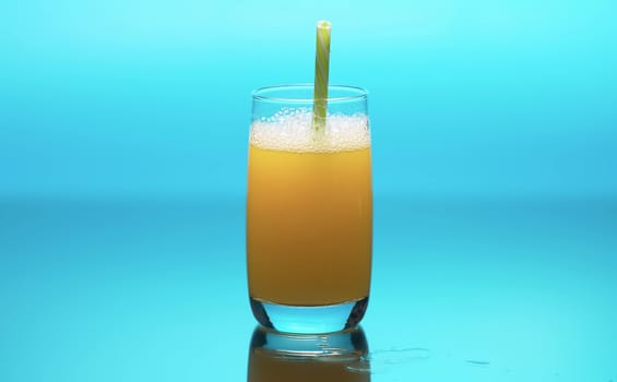 Fresh orange juice in a transparent glass on a table. Close up refreshing yellow beverage on blue background. Healthy lifestyle concept