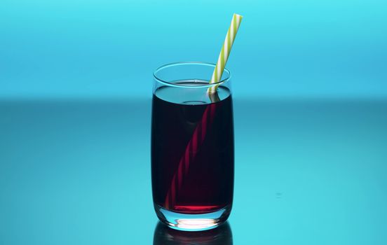 Close up cherry juice in the transperent drinking glass on blue bacground. Cherry or pomegranate or cranberry juice.