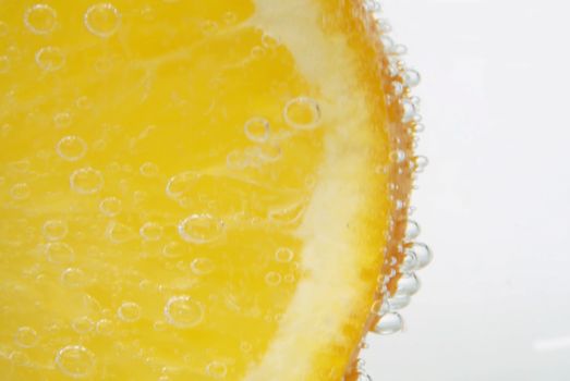 Macro shooting sliced orange in tonic, soda fizzy on a white background. Refreshing mineral water in a glass. Gas bubbles. Healthy drink