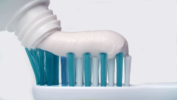 Toothpaste extruded onto a toothbrush. Dental health care or oral hygiene - Squeezing White Toothpaste From A Tube Onto A Toothbrush.