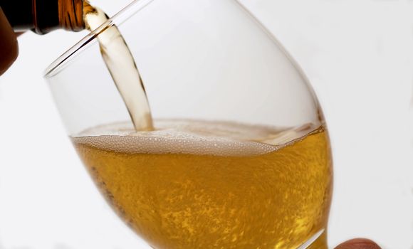 Close up of pouring beer from a bottle into a glass, low angle side view, white background. Bubbles rising up