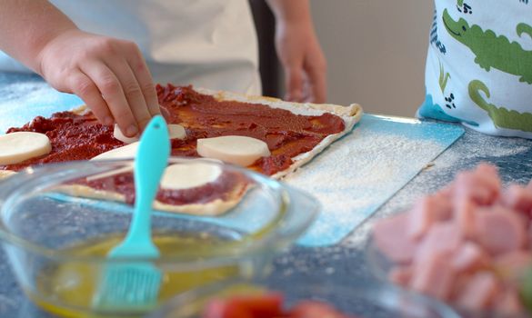 Close up hands of two young chefs making pizza. Siblings putting sliced cheese on rolled dough.