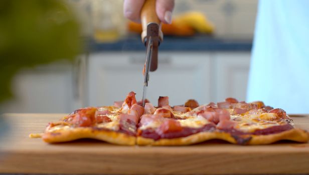 Close up female hands cutting pizza with roller knife on wooden board. Preparation of traditional italian food. Food concept.