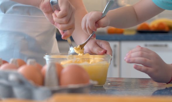 Close up hands of two children mixing butter with sugar and eggs in glass bowl. Childrens's hands cooking pastries.