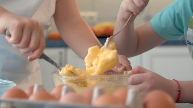 Close up hands of two children mixing butter with sugar and eggs in glass bowl. Childrens's hands cooking pastries.