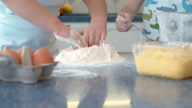 Close up hands of two children cooking pastry together in bright kitchen.