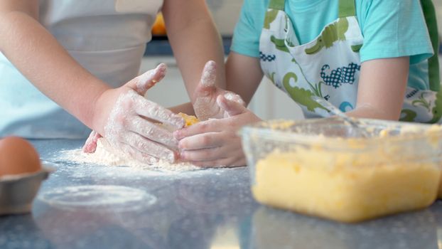 Close up hands of two children cooking pastry together in bright kitchen.