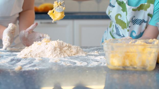 Close up hands of two children cooking pastry together in bright kitchen.