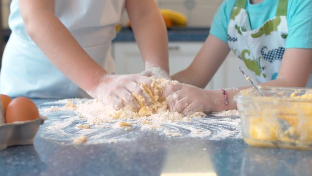 Close up hands of two children cooking pastry together in bright kitchen.