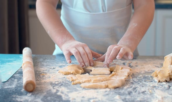 Close up hands of a girl making cookies with a cookie cutter. Children cooking pastry in bright kitchen