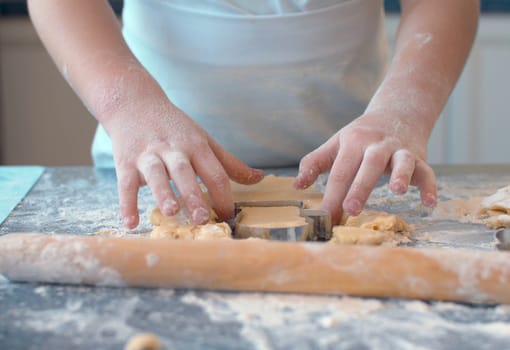 Close up hands of a girl making cookies with a cookie cutter. Children cooking pastry in bright kitchen