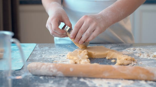 Close up hands of a girl making cookies with a cookie cutter. Children cooking pastry in bright kitchen