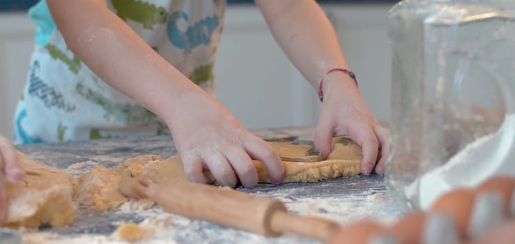 Close up hands of a boy making cookies with a cookie cutter. Child cooking pastry in bright kitchen
