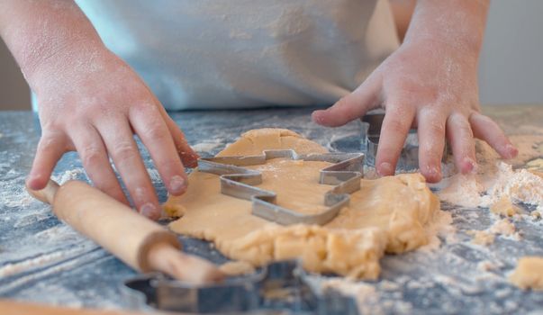 Close up hands of a girl making cookies with a cookie cutter. Children cooking pastry in bright kitchen