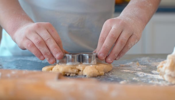 Close up hands of a girl making cookies with a cookie cutter. Children cooking pastry in bright kitchen