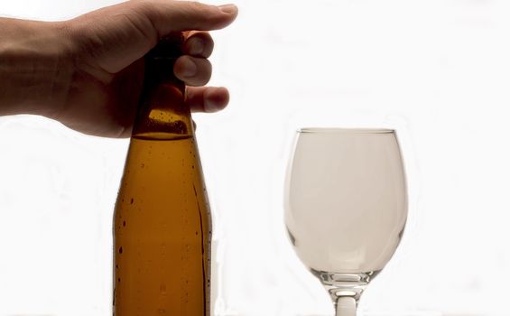 Close up male hand putting misted bottle of cold beer on the table. White background. Drops of water flowing down. Craft beer closeup
