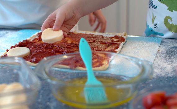 Close up hands of two young chefs making pizza. Siblings putting sliced cheese on rolled dough.