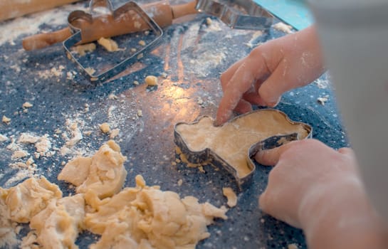 Close up hands of a girl making cookies with a cookie cutter. Children cooking pastry in bright kitchen