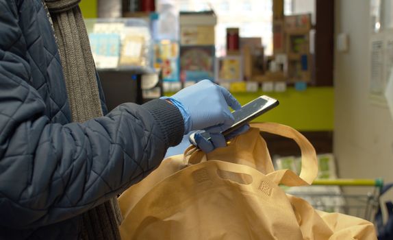 Man in latex blue gloves scrolling a smart phone in a supermarket. Close up male hands. Concept of healthy and safety life. Epidemic, quarantine, coronavirus