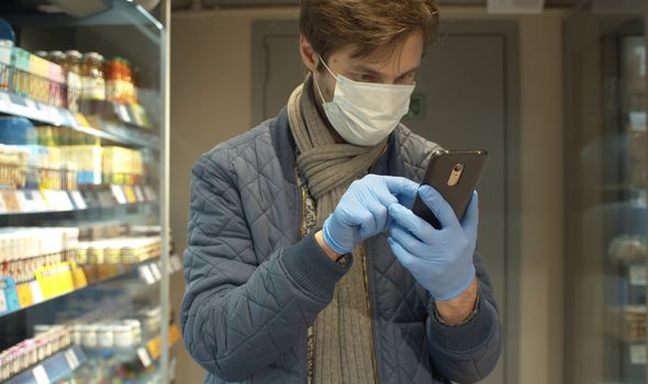 Handsome man in casual clothes in the supermarket. He is looking in the smartphone. Coronavirus epidemic in the city.