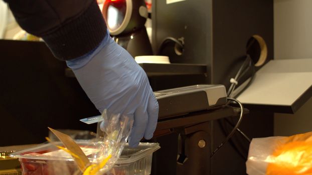 Close up hand of a man swiping debit card on pos terminal at self checkout counter inside foods store. Male hand in latex gloves paying by credit card during coronavirus epidemic