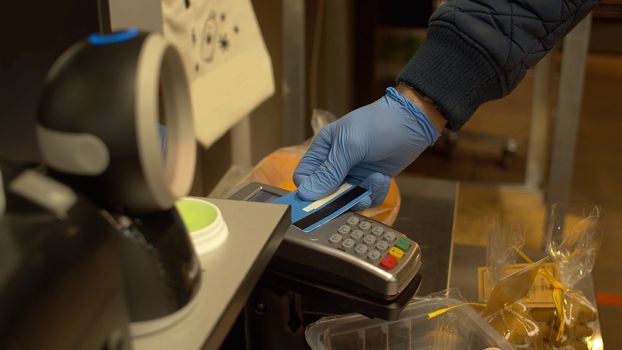 NFC technology credit card payment. Male hand in protective gloves paying with contactless credit card. Banking services of electronic money. Wireless payment. Coronavirus epidemic in the city.