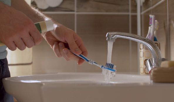 A young man brushes his teeth in a beautiful bathroom. Close up male hands with tooth paste and tooth brush. Daily Hygiene Procedures