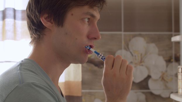 A young man brushes his teeth in a beautiful bathroom. Close up male portrait. Daily Hygiene Procedures