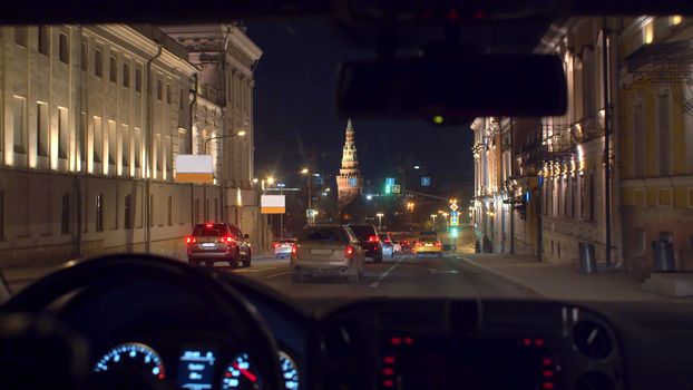 RUSSIA MOSCOW november 2019 - Moscow Kremlin through the windshield at night. Point of view inside moving car. Close up man's hands on the steering wheel and instrument panel lights up.