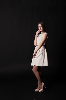 young beautiful girl in a bright dress posing standing in studio on black background