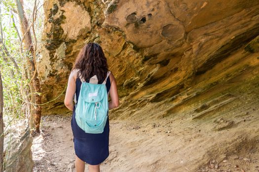 Young woman walking under a big rock carrying a blue bag