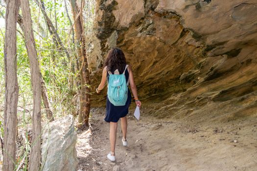 Young woman walking under a big rock carrying a blue bag