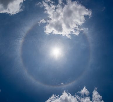 Photo of a solar halo visible in the sky. A color circle with the sun in the center and some cirrus clouds around it