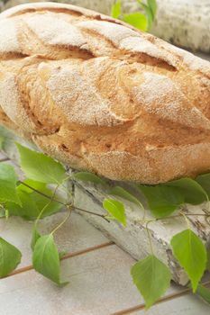 Fresh and delicious bread on wooden shabby cutting board and birch branch for healthy diet concept