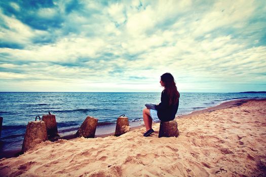 Emotion conceptual image. Sad lonely woman sitting on the beach. Instagram vintage picture.