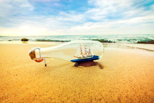 Bottle with ship inside lying on the beach. Souvenir conceptual image. Nature in paradise.