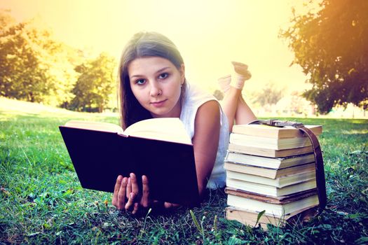Student girl reading a book on campus grass. Education conceptual image. Instagram vintage picture.