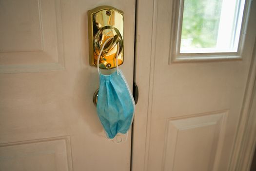 Blue mask hanging from lock as a reminder to wear facemask when leaving home to protect face, nose, and mouth from coronavirus