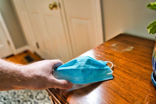 Hand grabbing mask off table looking towards door. Using mask as protecting from coronavirus to flatten the curve