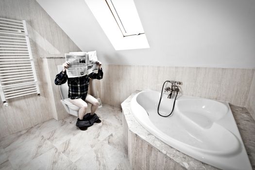Man is sitting on the toilet and reading the newspaper.
