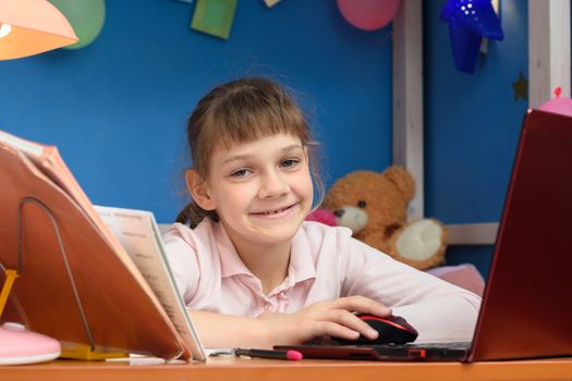 Happy girl works in a laptop in her children's room