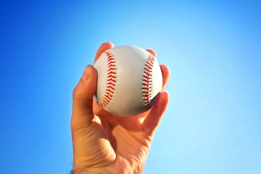 Baseball game. Baseball ball holding by hand against blue clean sky.