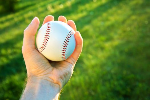 Baseball game. Baseball ball holding by hand against green fresh grass.
