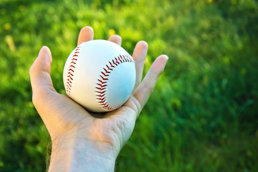 Baseball game. Baseball ball holding by hand against green fresh grass.