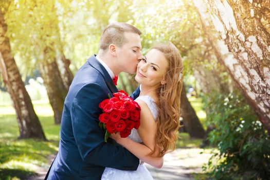Wedding Couple with red rose bouquet in green park at summer. Marriage and wedding concept image.