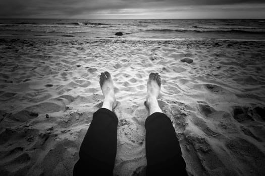 Destination place. Man sitting on the dark beach near ocean. Black and white image.