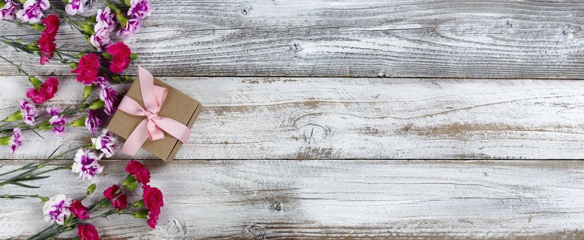 Left side border of carnation flowers and Mothers day gift box on white rustic wooden background with copy space. Top view in flat lay format.   