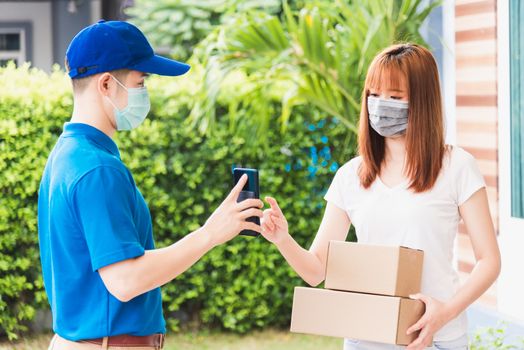 Asian delivery express courier young man giving parcel boxes to woman customer signature for receiving on mobile phone both protective face mask, under curfew quarantine pandemic coronavirus COVID-19